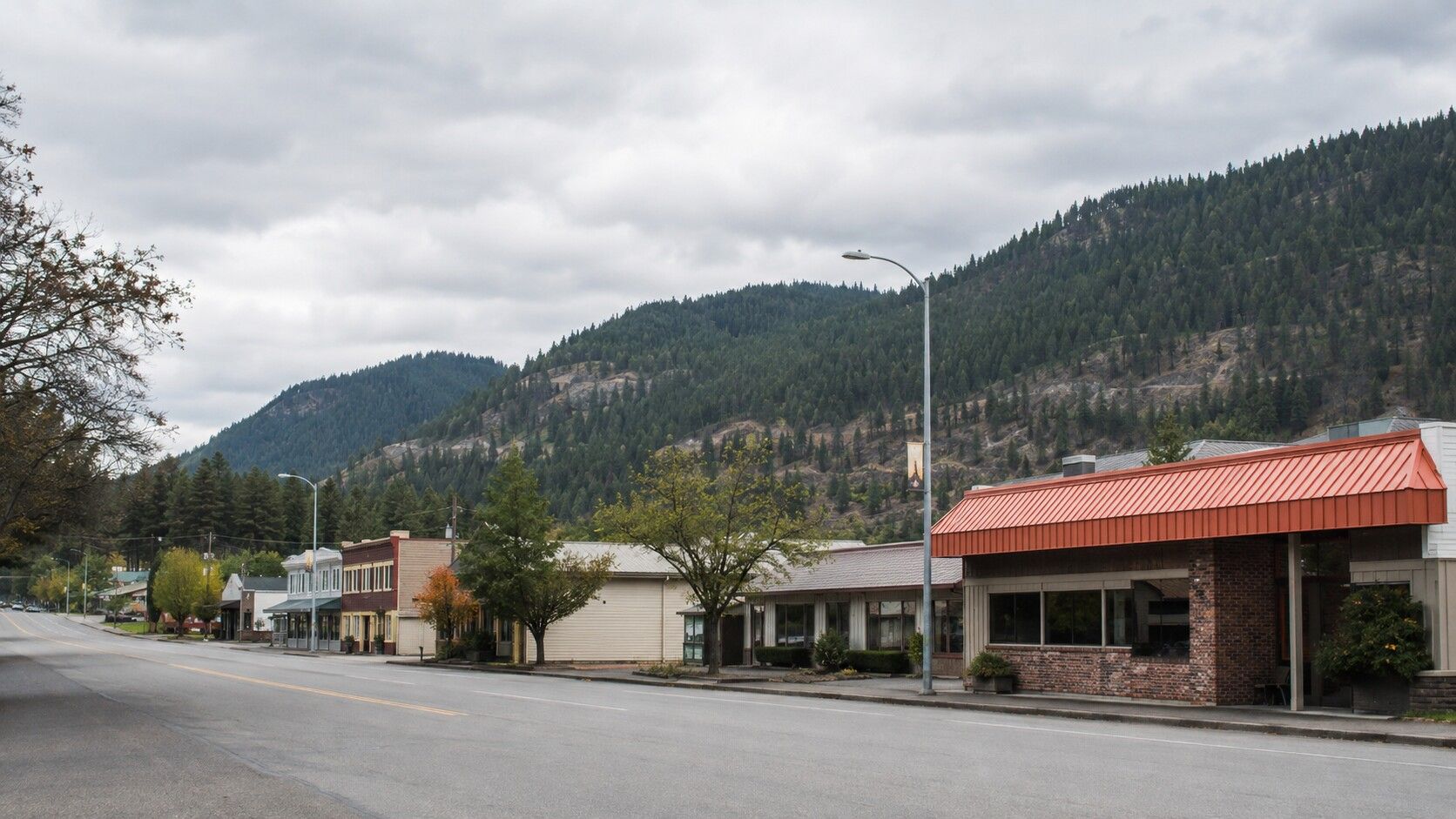 A small downtown street lined with shops, set against forested hills